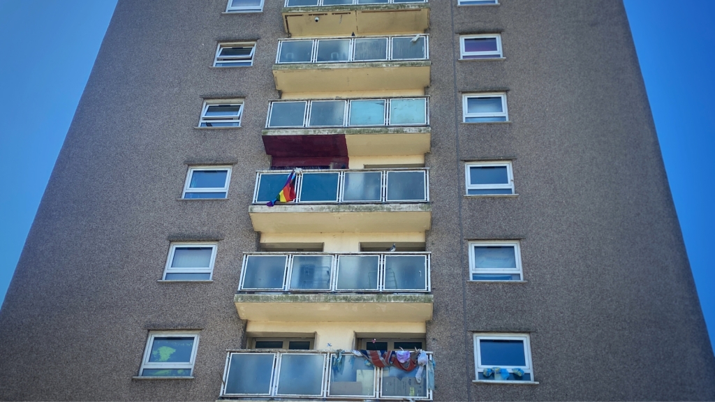 A pride flag hanging from a tower block balcony. 